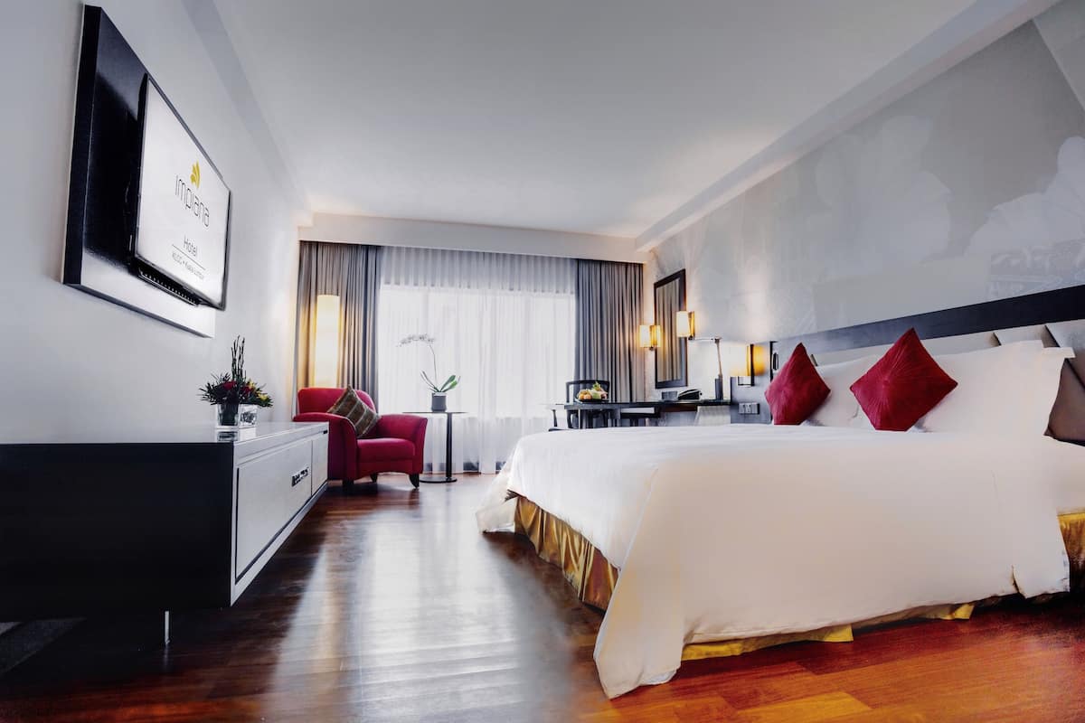 Een hotelkamer met een groot bed, een bureau, een rode stoel en een aan de muur bevestigde televisie.