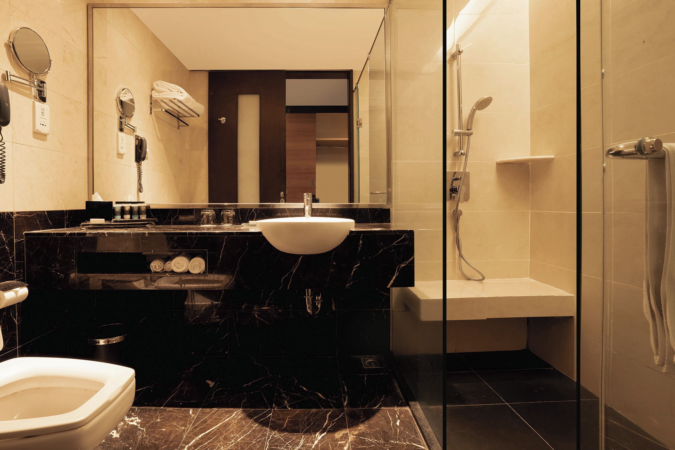 A modern bathroom with a black marble sink, a glass-enclosed shower, and a large mirror.