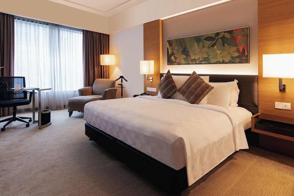 Een hotelkamer met een groot bed, twee bedlampen, een bureau met stoel, een televisie en een groot raam met gordijnen.
