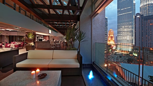 Un salón en la azotea con zona de estar acolchada, una mesita con velas y vistas a la ciudad.