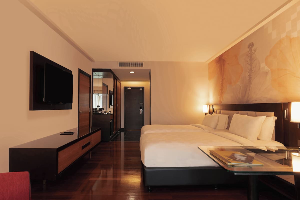 Een hotelkamer met een groot bed, een aan de muur bevestigde televisie, een bureau met stoel en een schilderij.