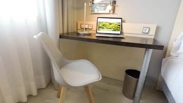 Una habitación de hotel pequeña y moderna con escritorio, una computadora portátil, una silla, una cama y un cesto de basura.