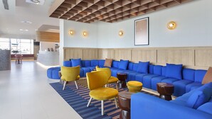 A modern lobby with a blue sectional sofa, yellow chairs, and a patterned rug. - Holiday Inn Express Pamplona by IHG (Aranguren)