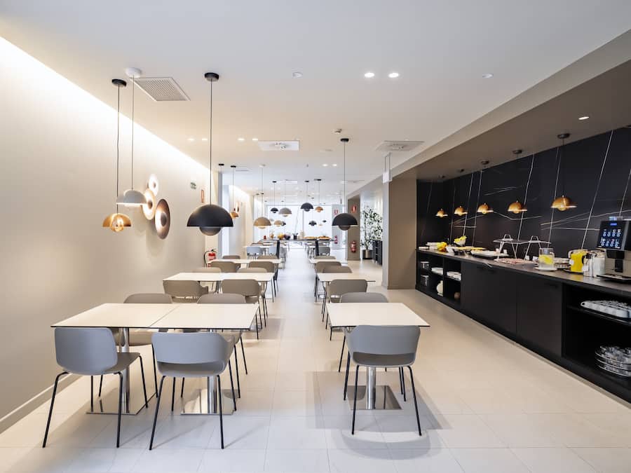 A modern dining area with tables and chairs, a kitchen counter with appliances, and pendant lighting.
