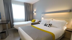 A hotel room with two single beds, a desk, a chair, a trash bin, and a bedside table with a lamp. - Holiday Inn Express Pamplona by IHG (Aranguren)