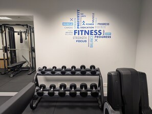 Een sportschool met een muur vol motiverende woorden, een bank en een rek met gewichtsschijven.