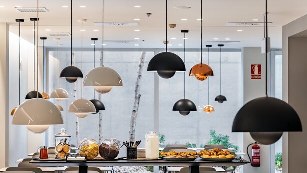 A modern dining area with multiple tables, hanging pendant lights, and a view of the outdoors. - Holiday Inn Express Pamplona by IHG (Aranguren)