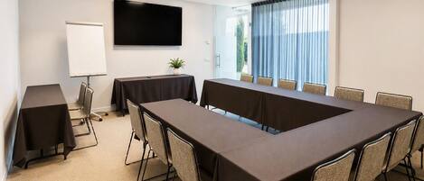 Un salón de conferencias con una larga mesa, sillas, una pizarra y una pantalla de televisión.