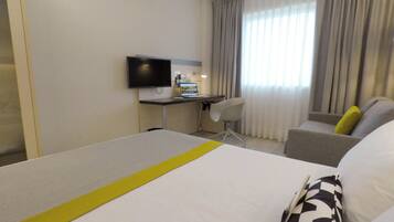 A hotel room with a bed, a desk, a chair, a television, and a window with curtains.