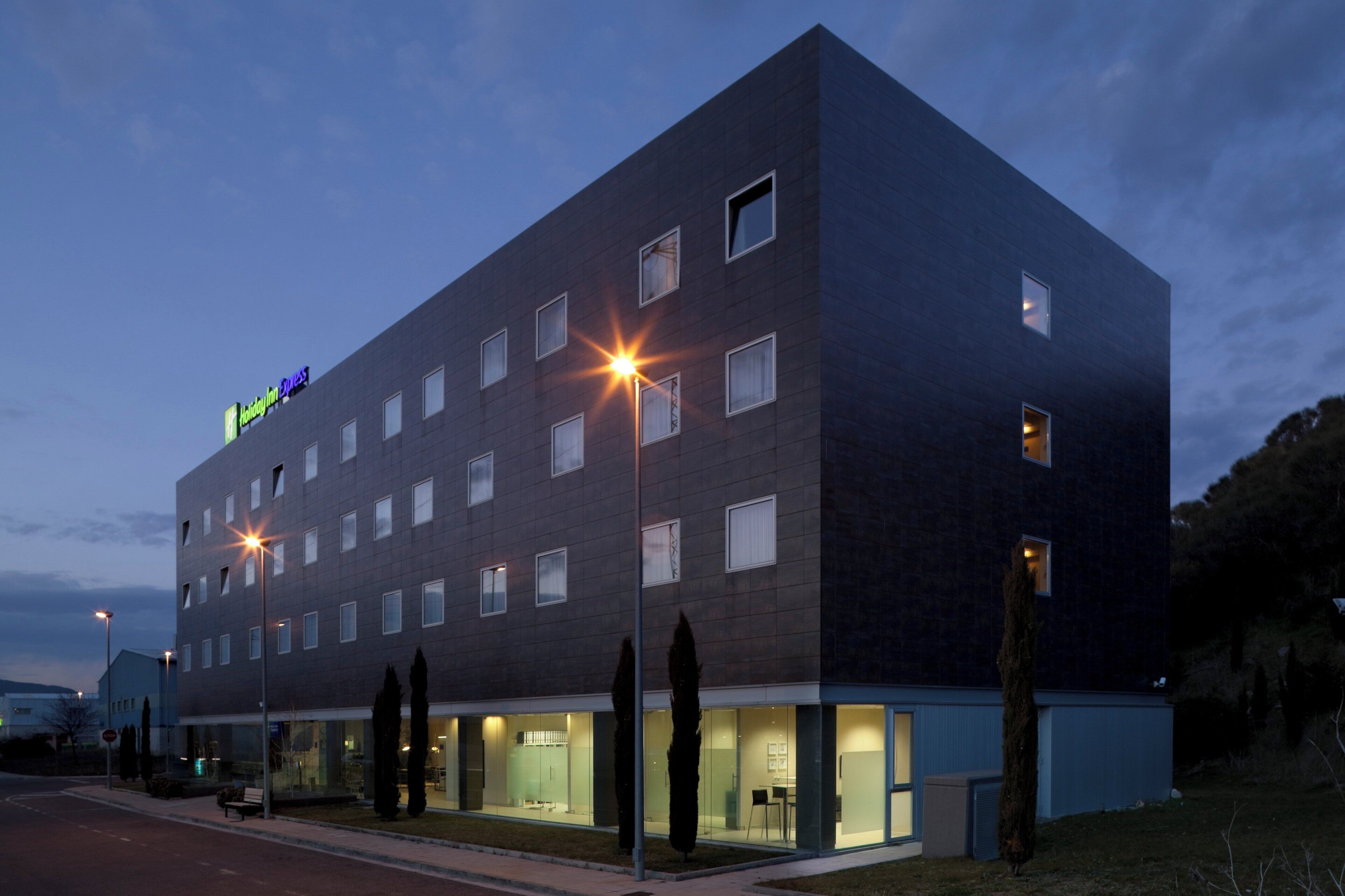 Un hôtel moderne, avec un bâtiment à la façade plate, de nombreuses fenêtres et une entrée bien visible, dotée de portes en verre.