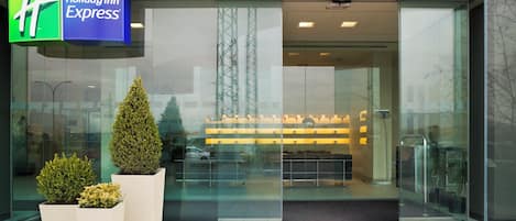 Entree van een Holiday Inn Express hotel met een glazen gevel, plantenbakken en zichtbare inrichting met zitplaatsen.