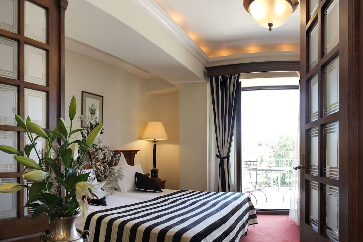 Une chambre d’hôtel avec un grand lit, une table de chevet avec une lampe, une plante en pot et une vue sur l’extérieur grâce à une grande fenêtre.