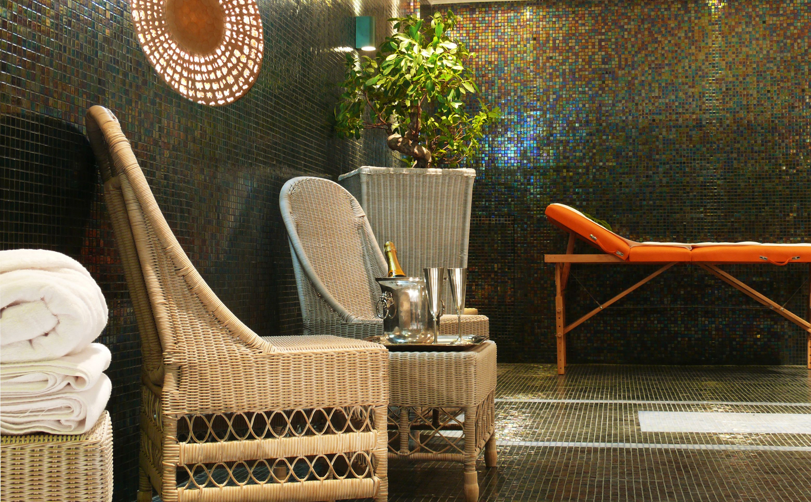 Un espace de détente avec des fauteuils en osier, une chaise longue, une plante en pot et un mur décoratif.