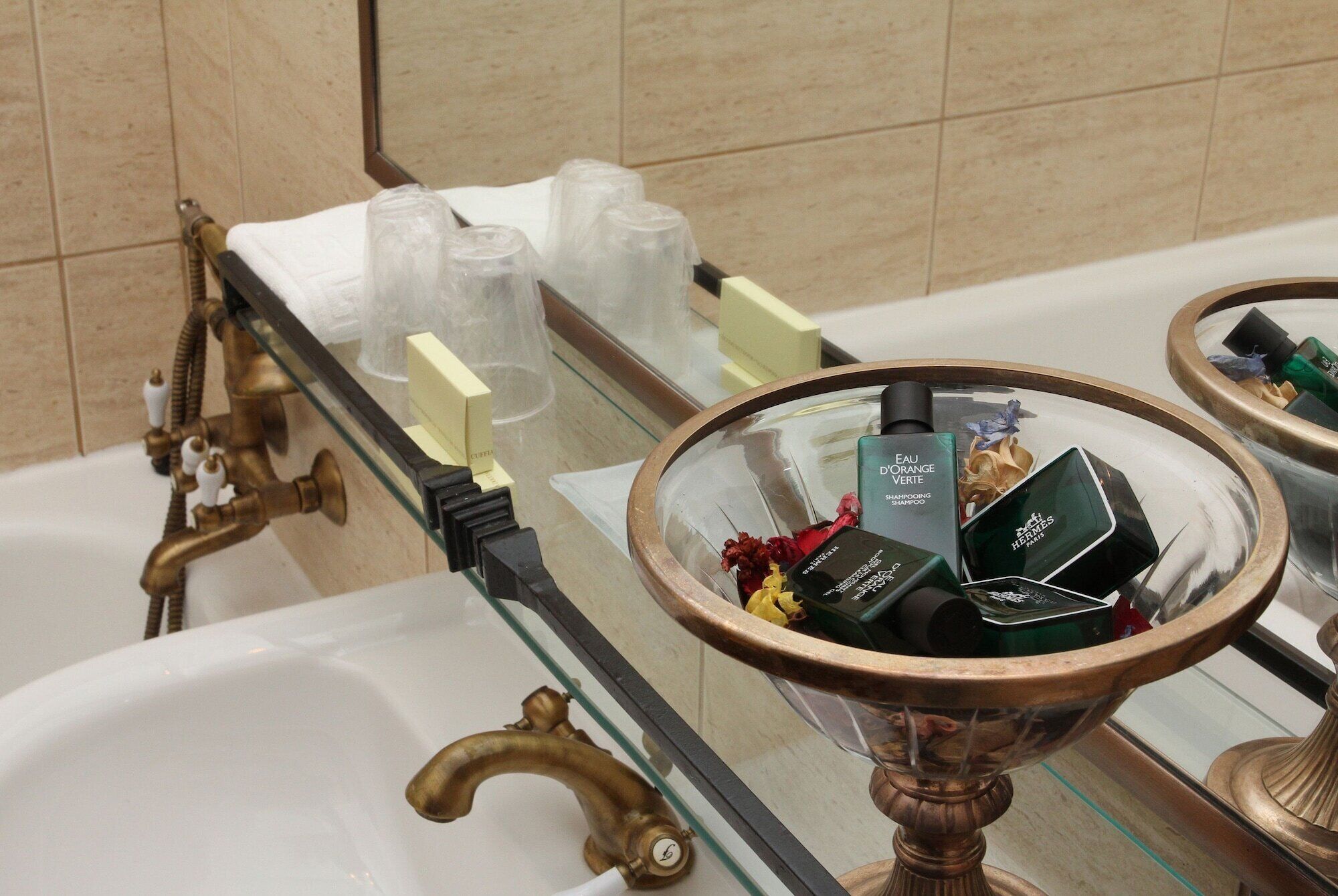 Une salle de bain avec une baignoire, une étagère en verre où sont rangés les articles de toilette et un miroir qui reflète la pièce.