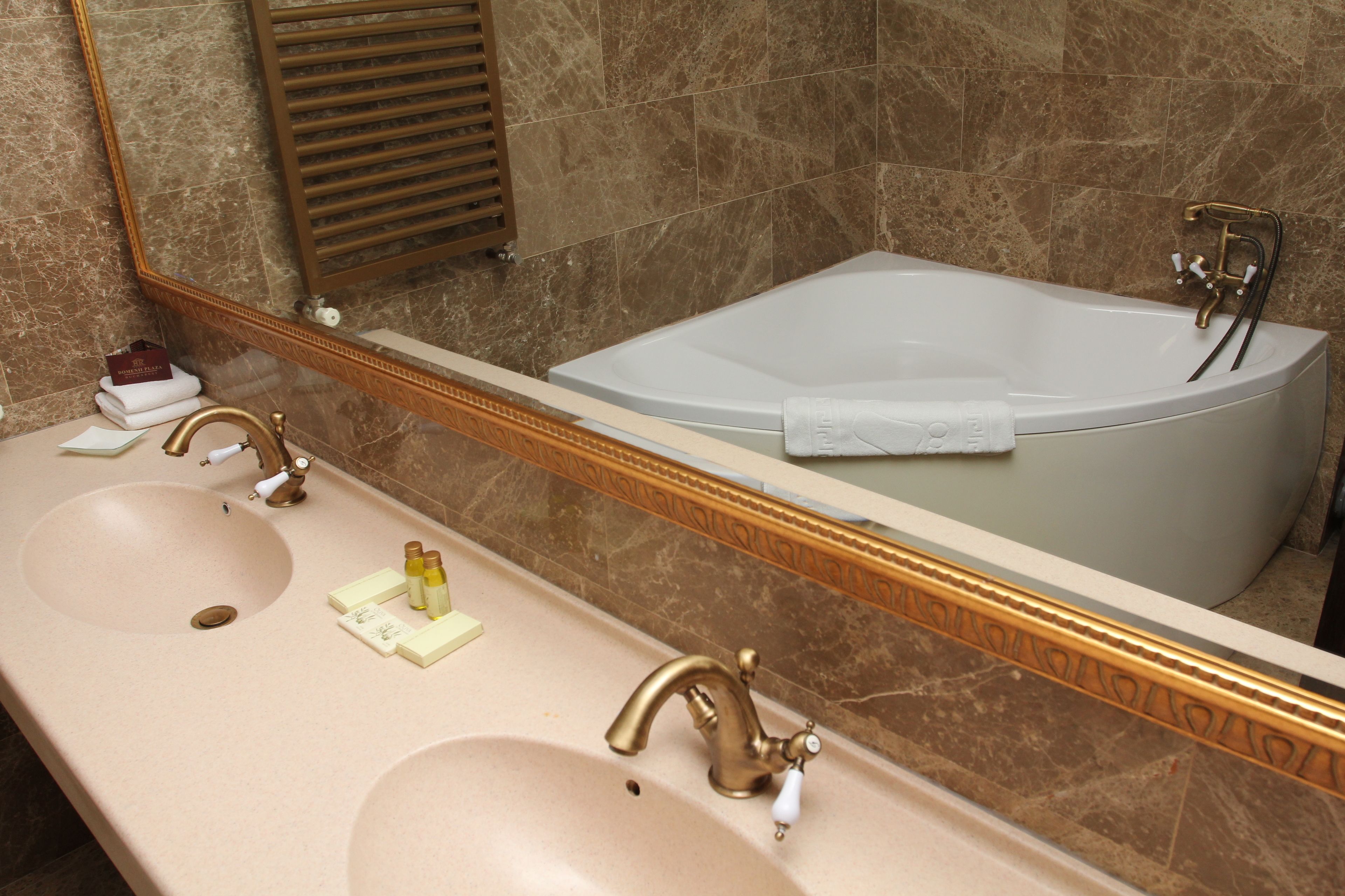 A bathroom with a large mirror, two sinks, a bathtub, and marble walls.