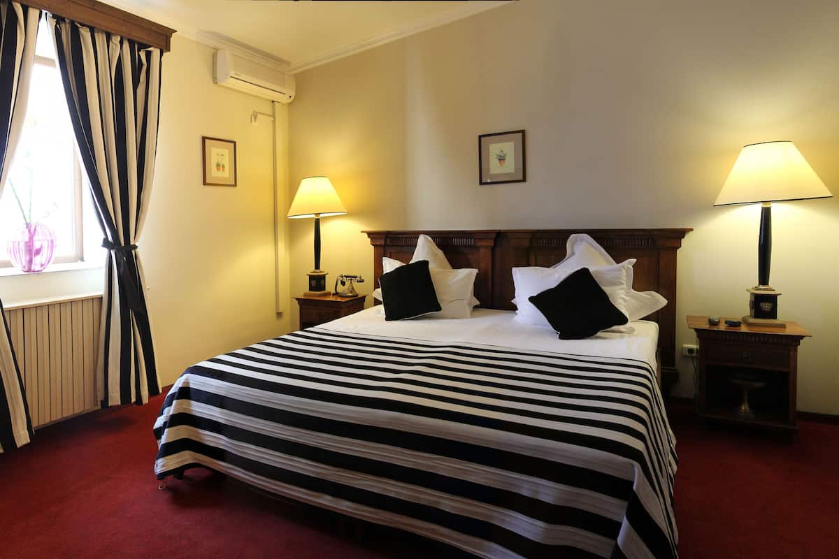 Une chambre d’hôtel avec un grand lit, deux tables de chevet, une fenêtre avec des rideaux et deux lampes fixées au mur.