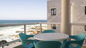En balkon med et bord og stole, med udsigt over en stenstrand og havet.