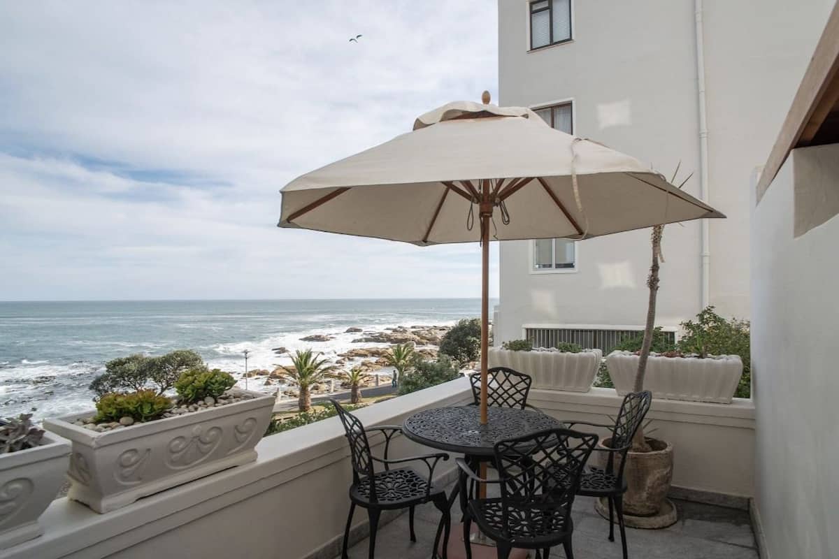 A balcony with a table and chairs, a large umbrella, and a view of the ocean.