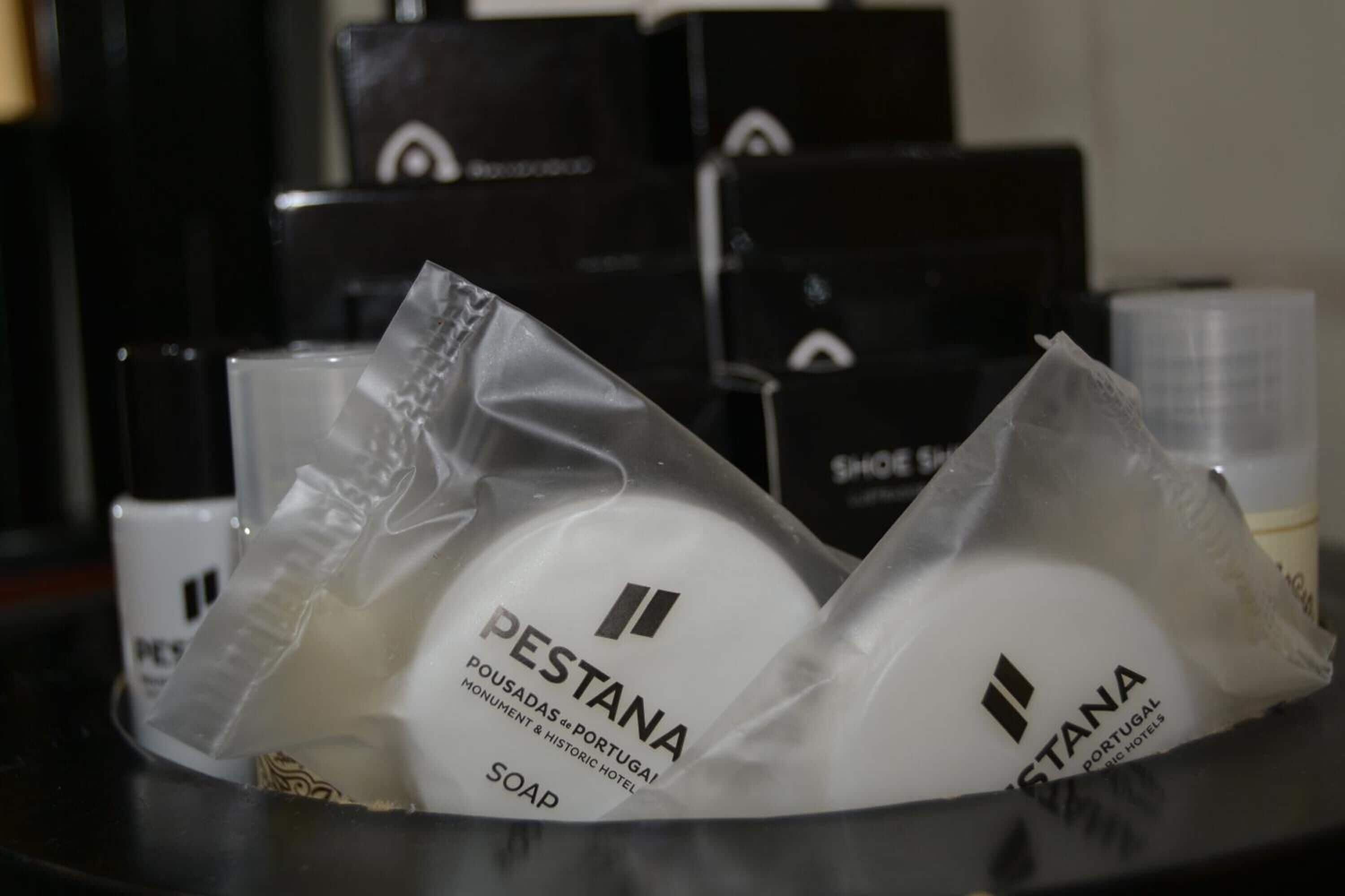 Une présentation des produits de savon PESTANA dans des emballages transparents, avec des boîtes noires en arrière-plan.