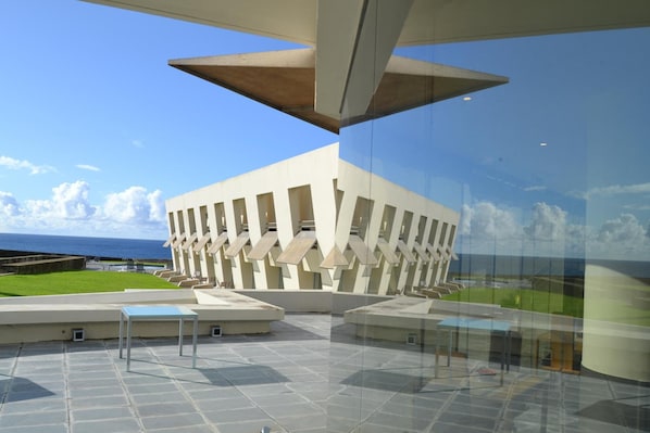 A modern building with a unique geometric design, large glass windows, and a view of the ocean.