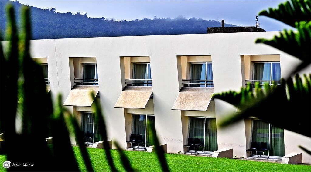 A modern building with multiple balconies, a flat roof, and a view of a forested hill.