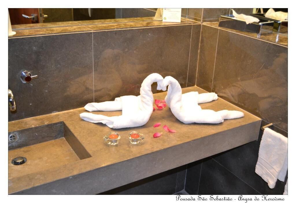 A bathroom with a stone sink, two swan-shaped towels, and rose petals.