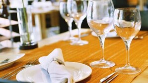 A dining table set with wine glasses, plates, and cutlery, with a plant in the background. - Pousada de Angra do Heroismo - Forte Sao Sebastiao (Angra do Heroismo)