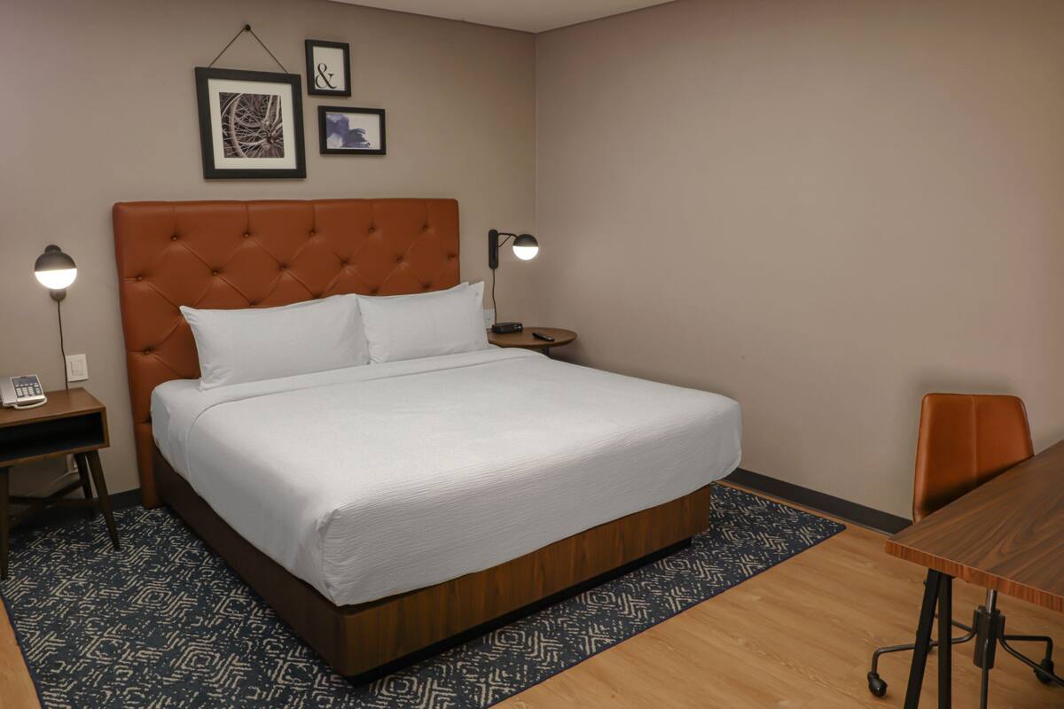 Habitación de hotel con una cama grande, un escritorio con lámpara, una silla y una mesita.