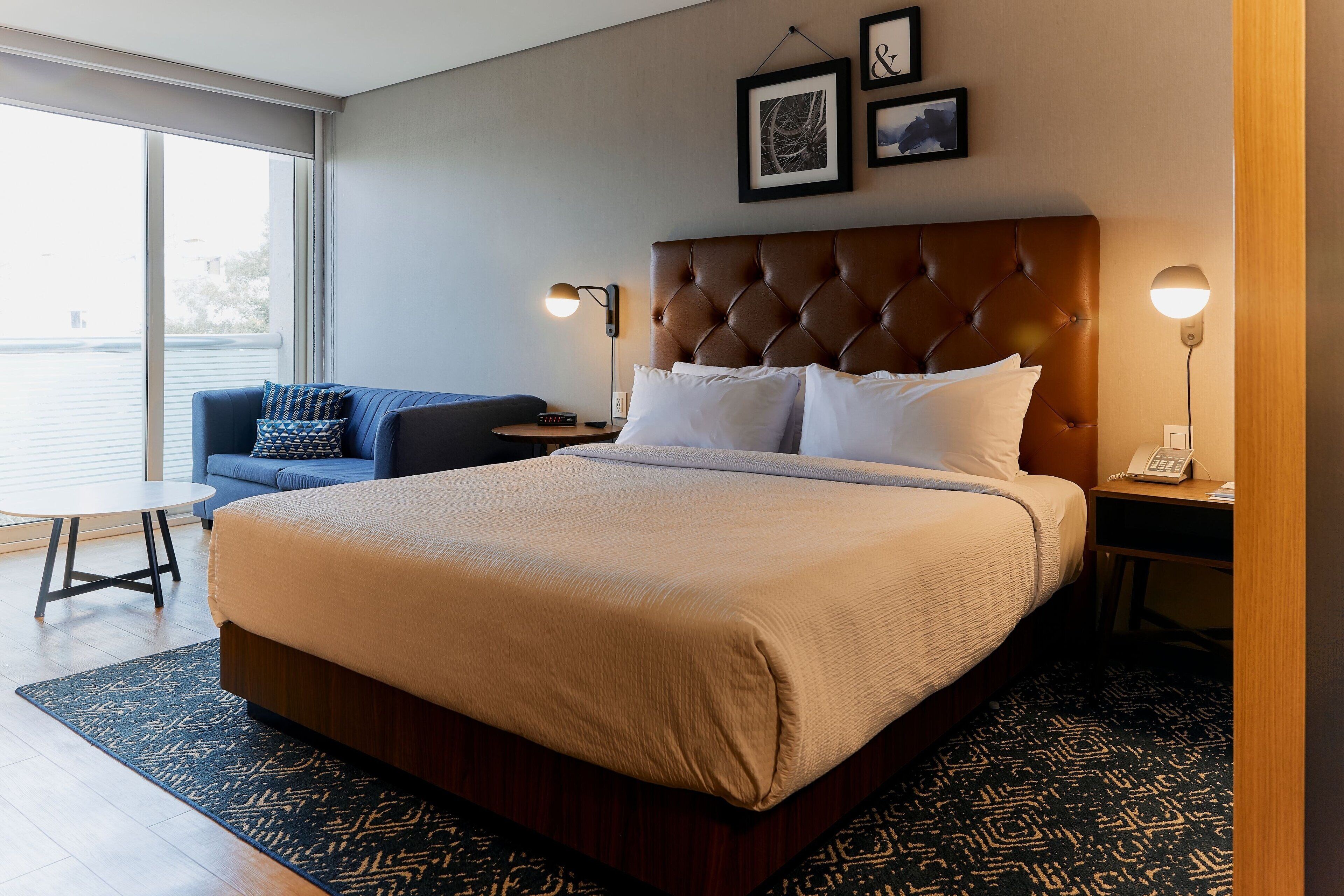 A hotel room with a large bed, a sofa, a small table, and a desk with a lamp.
