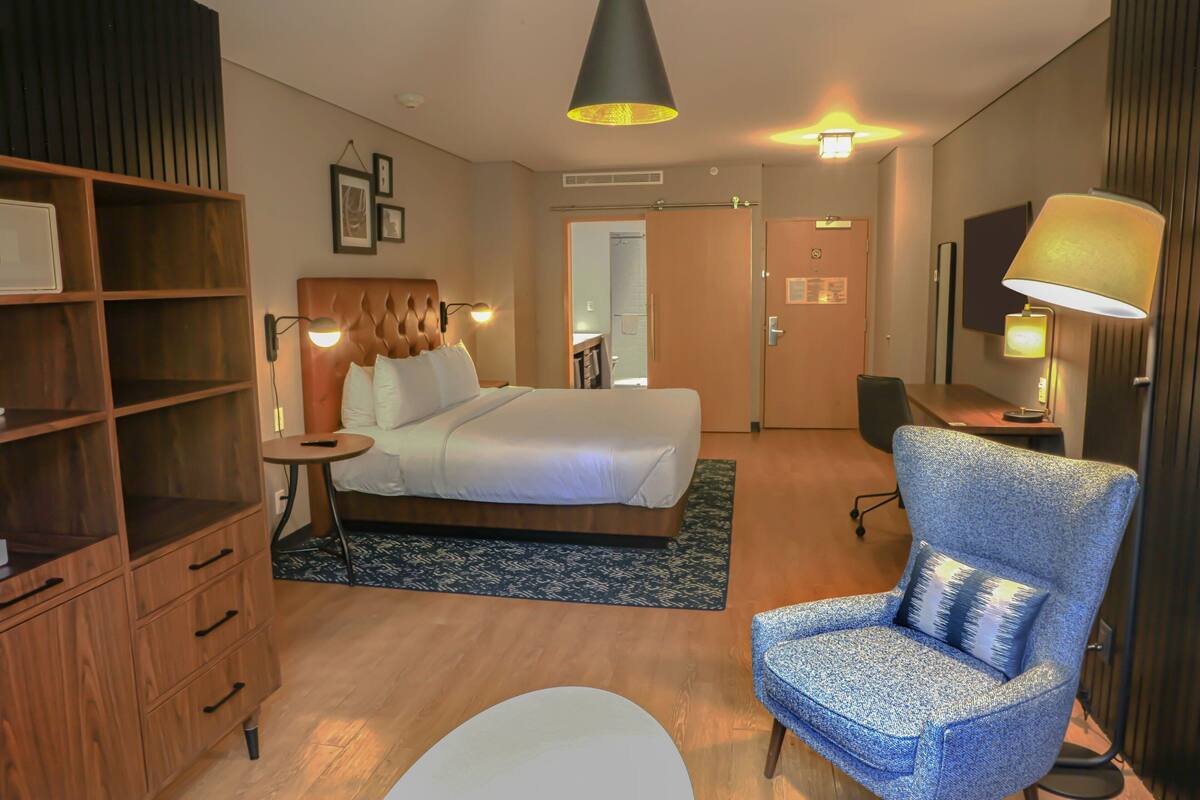Habitación de hotel con cama, escritorio, silla, armario y lámpara.