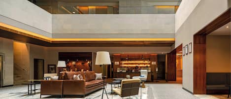 A spacious lobby with a high ceiling, a central seating area with sofas and chairs, a coffee table, and a large floor lamp.