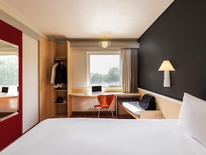 A hotel room with a bed, desk, chair, wardrobe, and a window with curtains. - ibis Guadalajara Expo (Guadalajara)