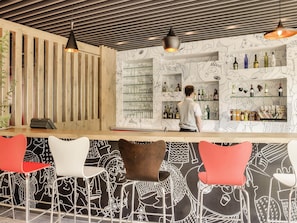 A bar area with a bartender, wooden slats, and patterned wall decor. - ibis Guadalajara Expo (Guadalajara)