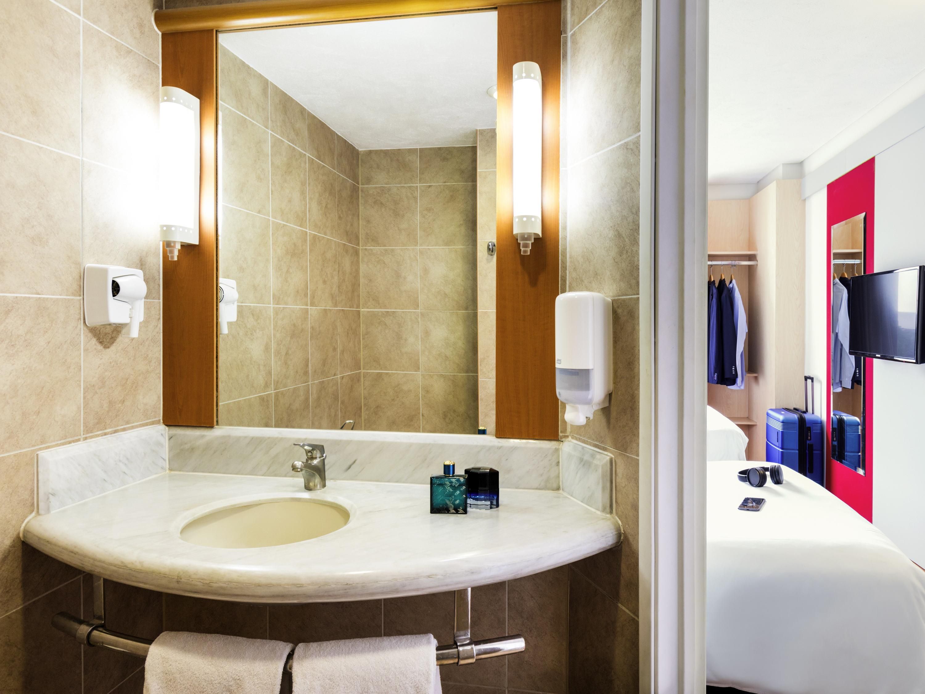A hotel bathroom with a sink, mirror, towel rack, and toiletries.