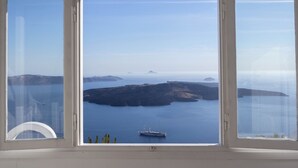A large arched window with a clear view of a calm sea, distant islands, and a ship. - Nomikos Villas (Santorini)