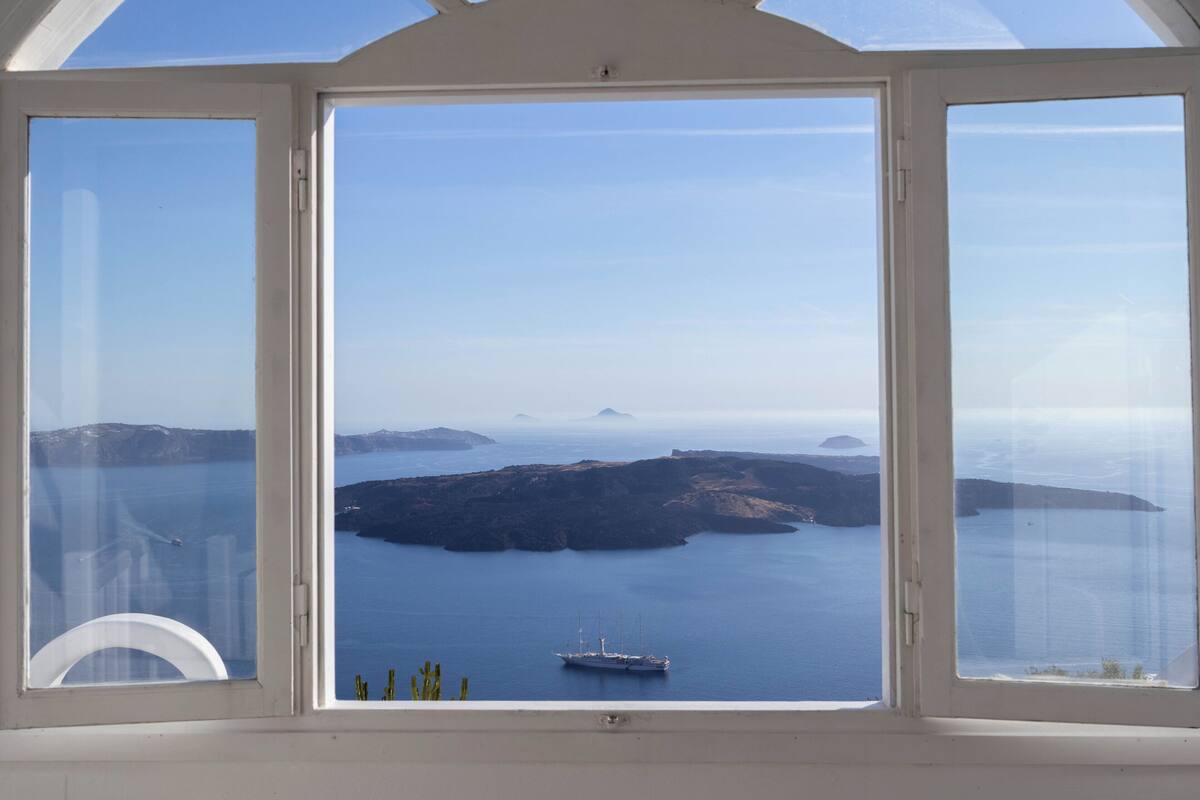 Un amplio ventanal arqueado con vistas despejadas al mar tranquilo, islas distantes y un barco.