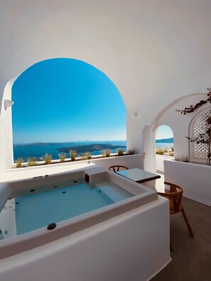 A modern outdoor hot tub area with a clear view of the sea and distant islands. - Nomikos Villas (Santorini)