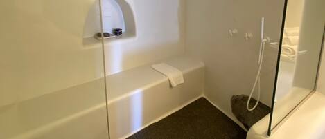 A modern bathroom with a glass shower enclosure, a white bathtub, and a small shelf with toiletries.