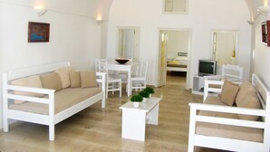 A spacious living room with white furniture, a dining area, and a TV. - Nomikos Villas (Santorini)