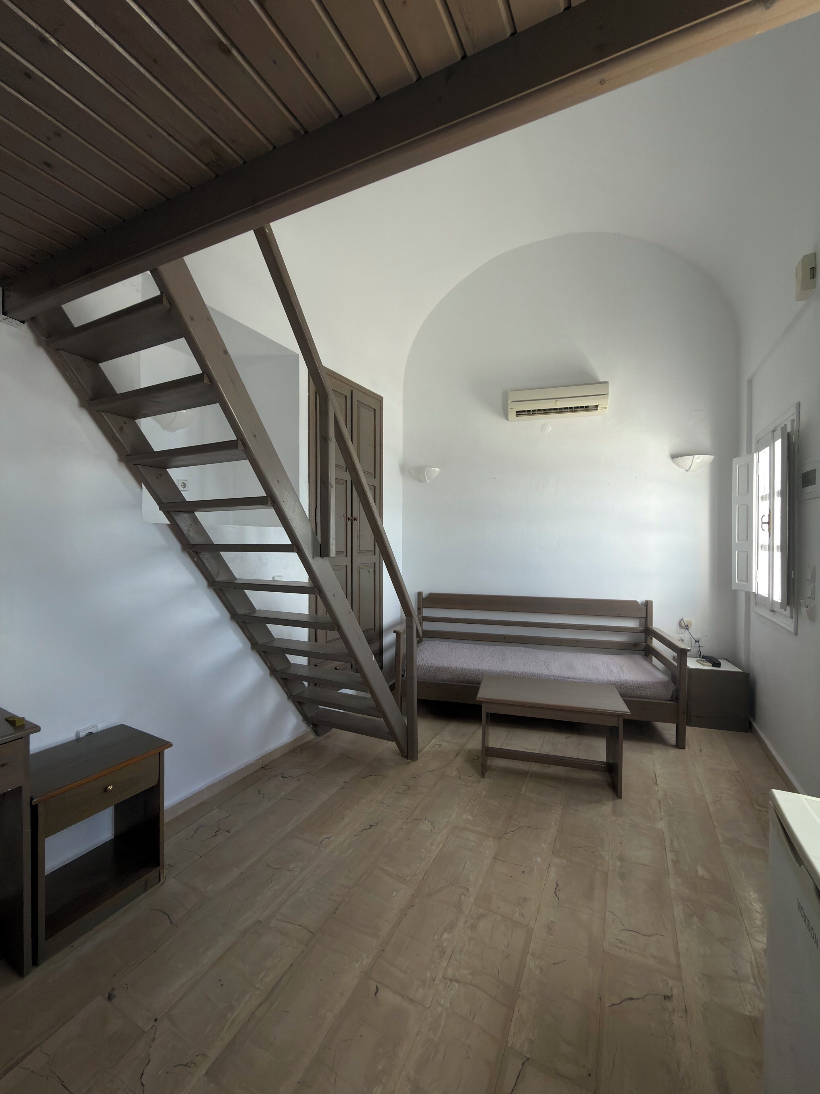 A room with a wooden bench, a small table, a ladder, and a staircase.