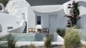A white-walled building with a pool, two wooden chairs, and a door. - Nomikos Villas (Santorini)