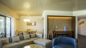 A modern living room with a sectional sofa, a blue armchair, a glass coffee table, a dining area with a wooden table and chairs, and a decorative wall panel.
