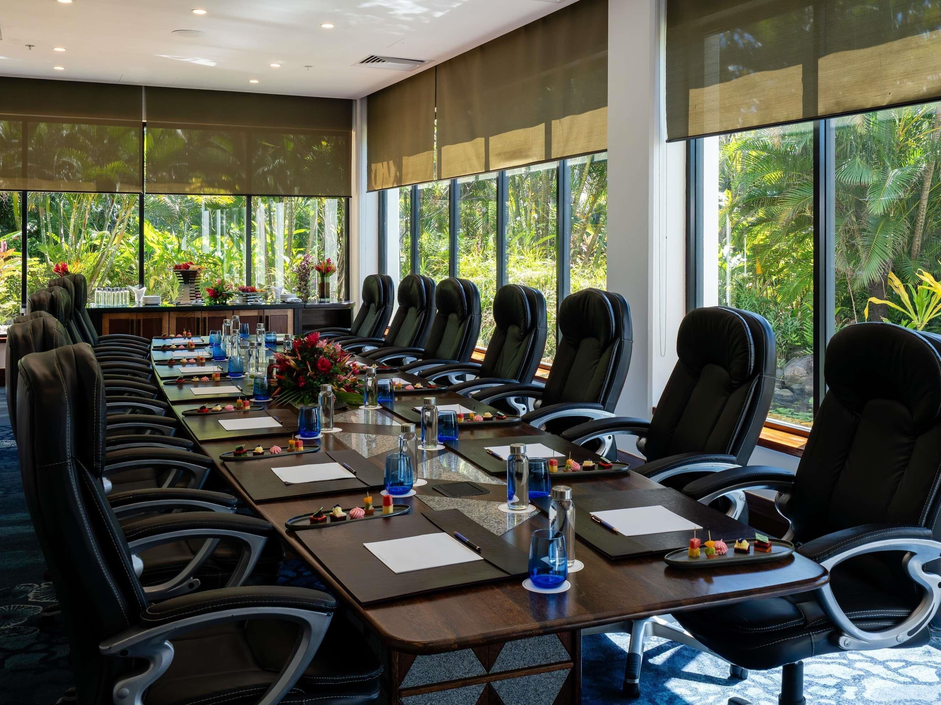 A conference room with a long table, multiple chairs, and large windows with a view of greenery.