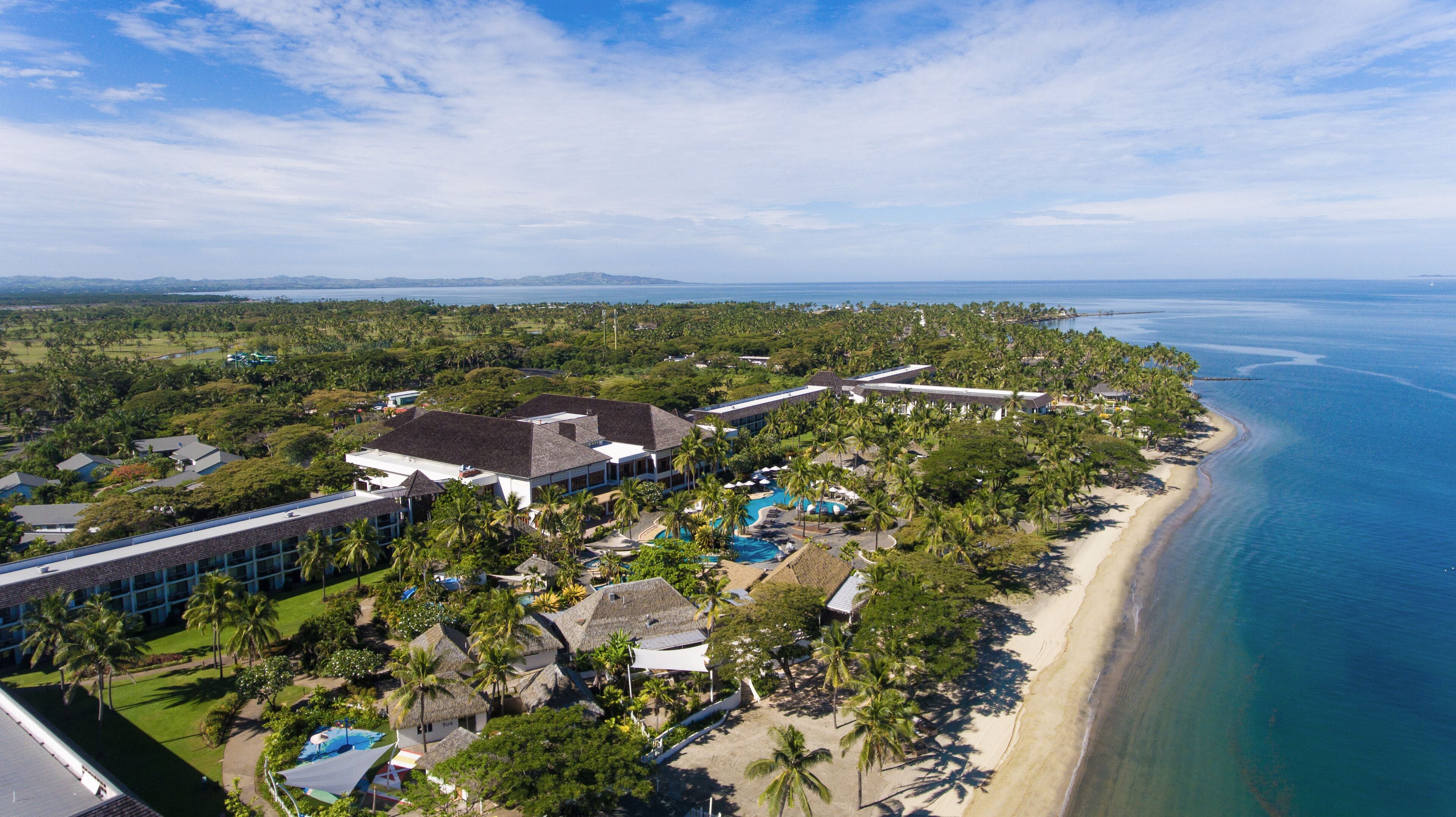 Vista aérea de un resort con playa, que incluye una piscina y varios edificios.