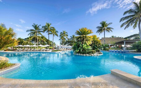 A pool surrounded by lounge chairs and palm trees.