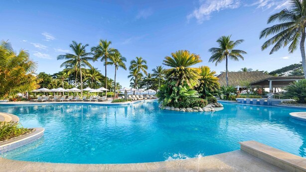 A pool surrounded by lounge chairs and palm trees.