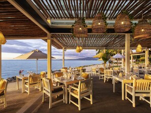 An outdoor dining area with tables and chairs, a pergola, hanging wicker lamps, and a view of the sea. - Sofitel Fiji Resort And Spa (Nadi)