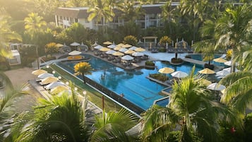 Ein Resort mit einem großen Schwimmbad, Liegebereichen inklusive Sonnenschirmen und Palmen.