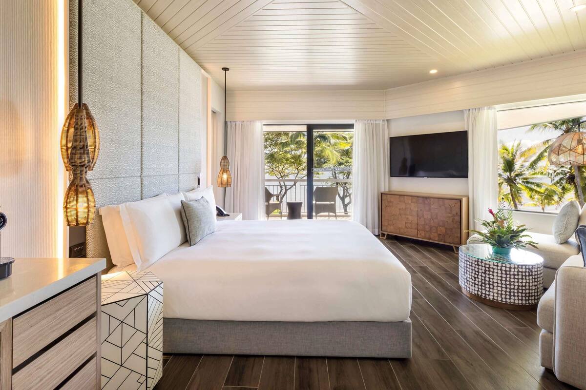 Une chambre d’hôtel moderne dotée d’un grand lit, d’une télévision, d’un balcon avec coin salon extérieur et d’un plafond en bois.
