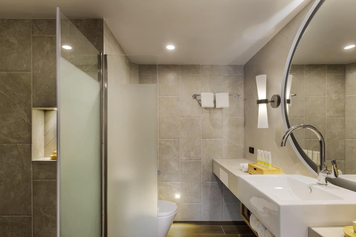 A modern bathroom with a glass shower enclosure, a white toilet, a large white sink with a mirror, and a wooden vanity.